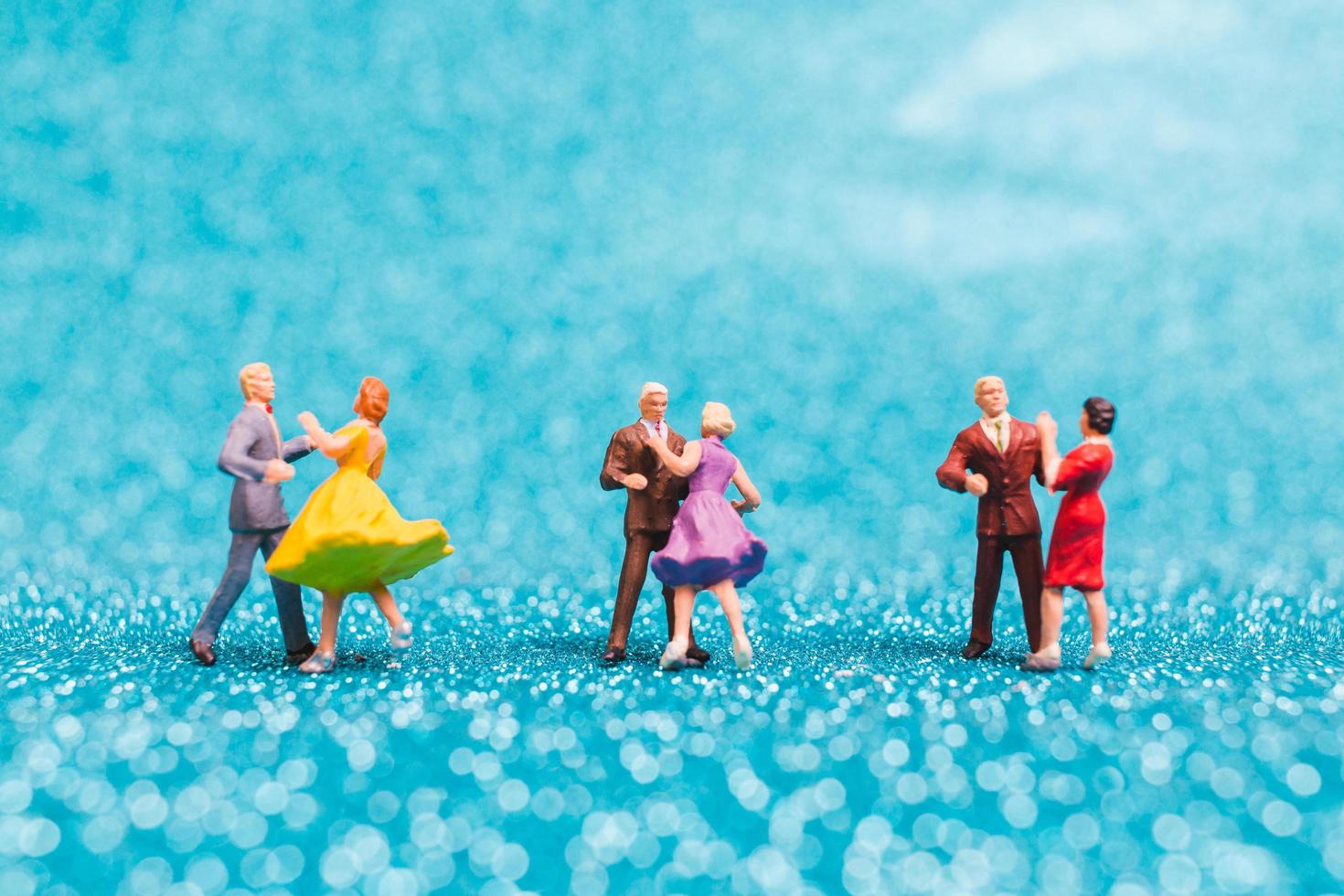 Miniature couples dancing on blue glitter background, Valentine's Day concept photo