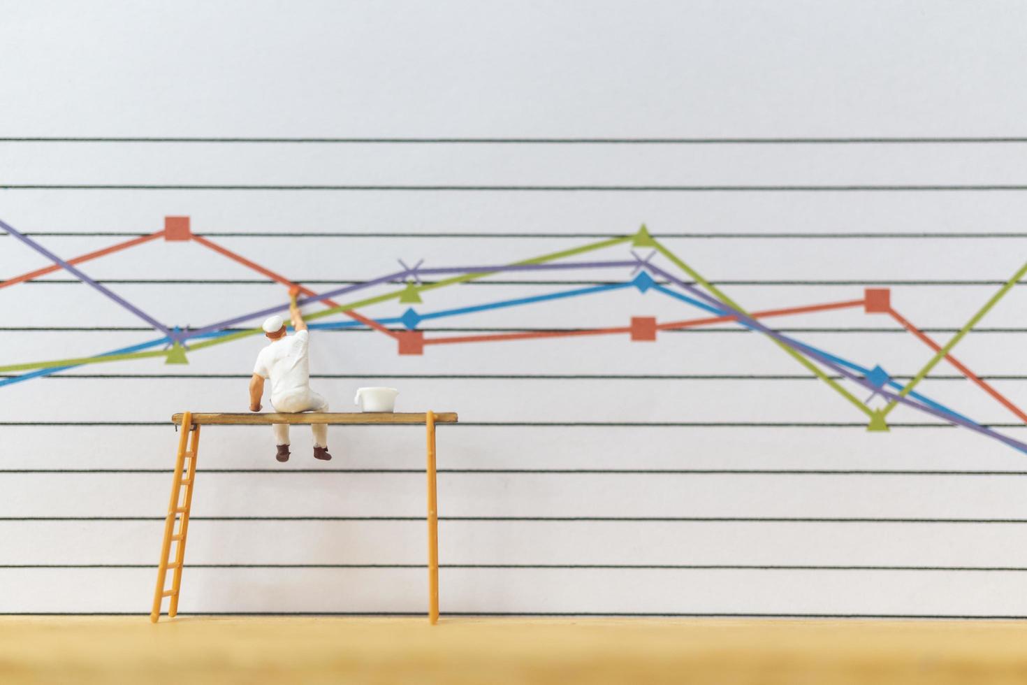 Miniature worker painting business graphs on a white background, business growth concept photo