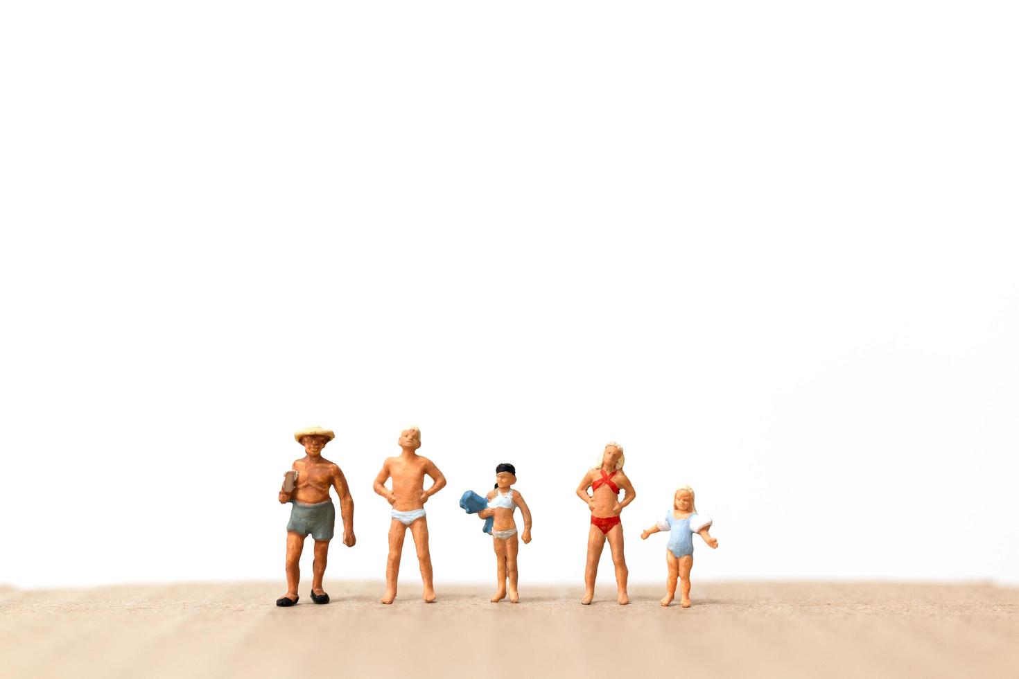 Miniature people wearing swimsuits standing on the beach, vacation concept photo