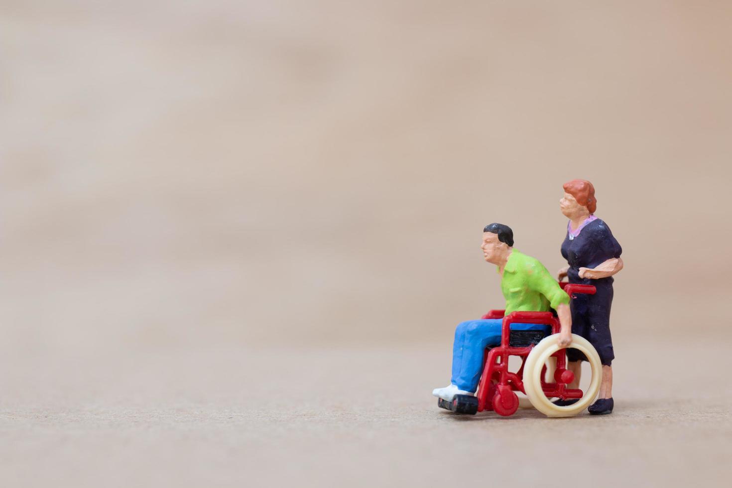 Miniature disabled man sitting in a wheelchair on a wooden background photo