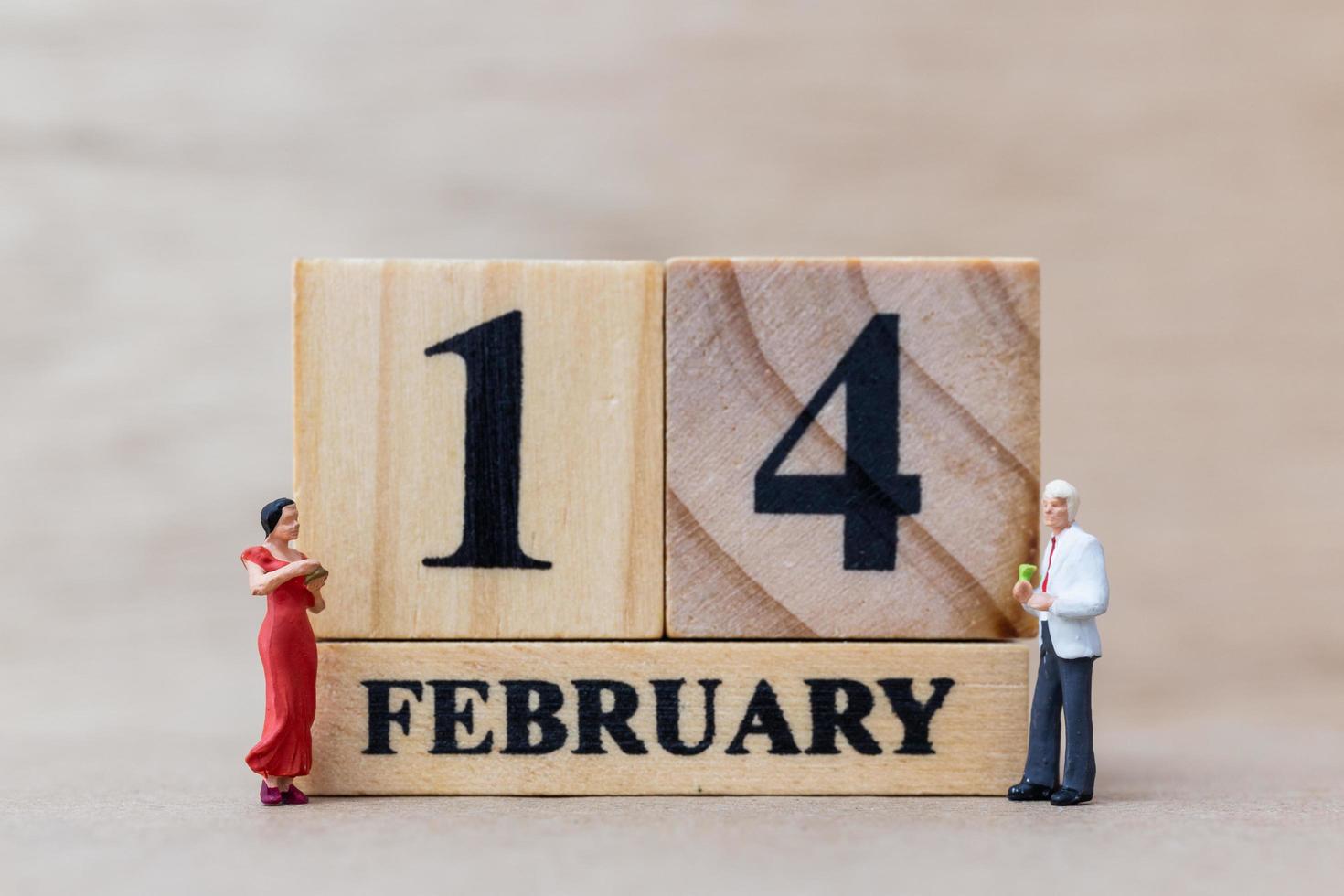 Miniature couple with wooden blocks 14 February text on a wooden background, Happy Valentine's Day concept photo