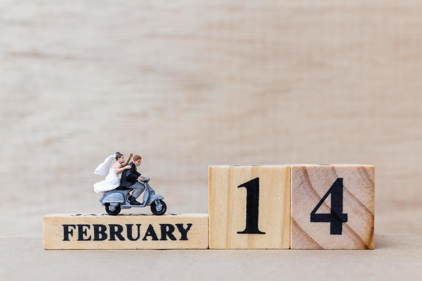 Pareja en miniatura con bloques de madera, texto del 14 de febrero sobre un fondo de madera, feliz día de San Valentín concepto foto