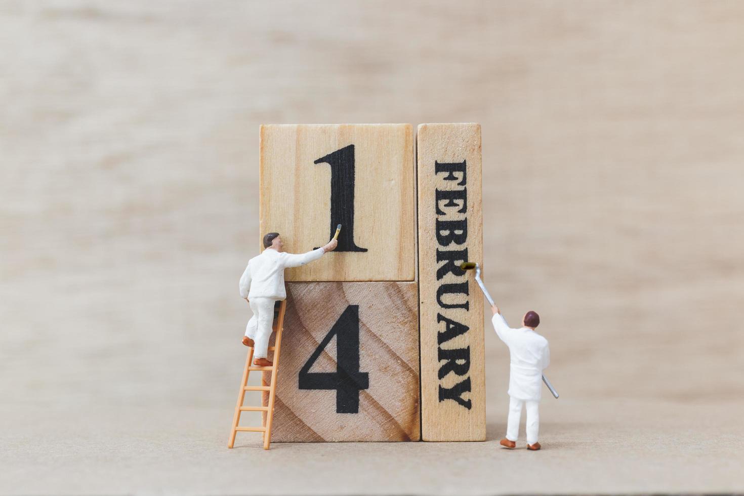 Miniature people painting wooden blocks with 14 February on a wooden background, Happy Valentine's Day concept photo