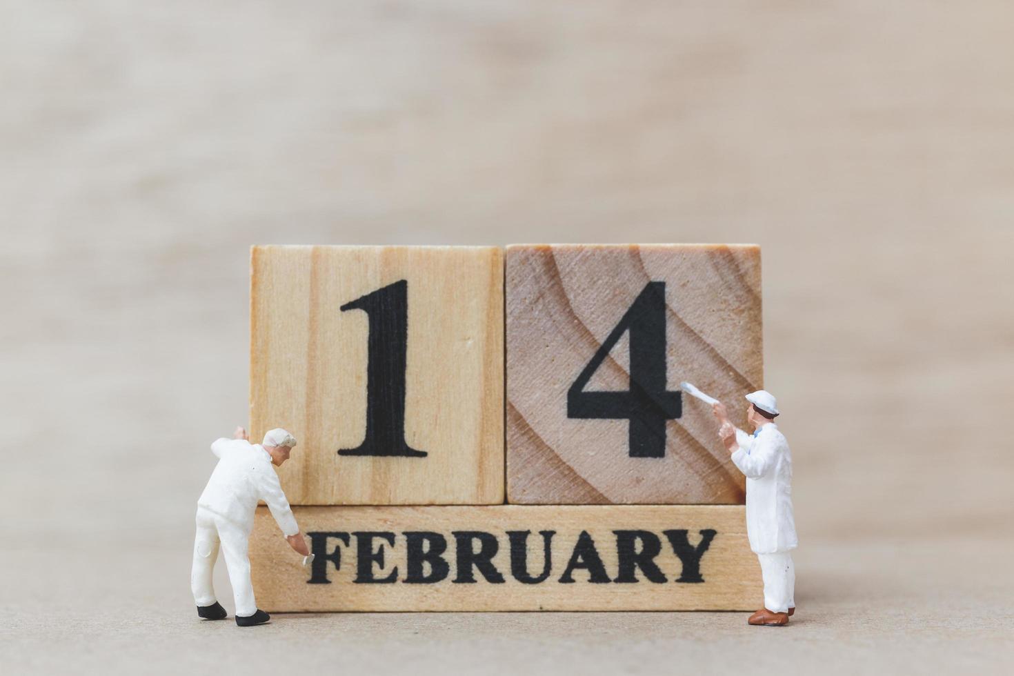 Gente en miniatura pintando bloques de madera con el 14 de febrero sobre un fondo de madera, feliz día de San Valentín concepto foto