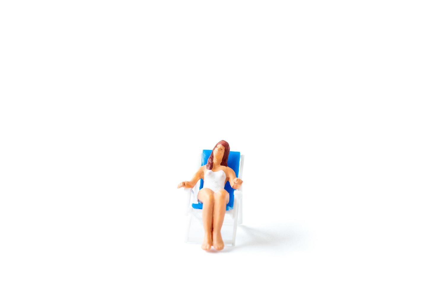 Miniature person sunbathing on a deck chair on a white background, summertime concept photo