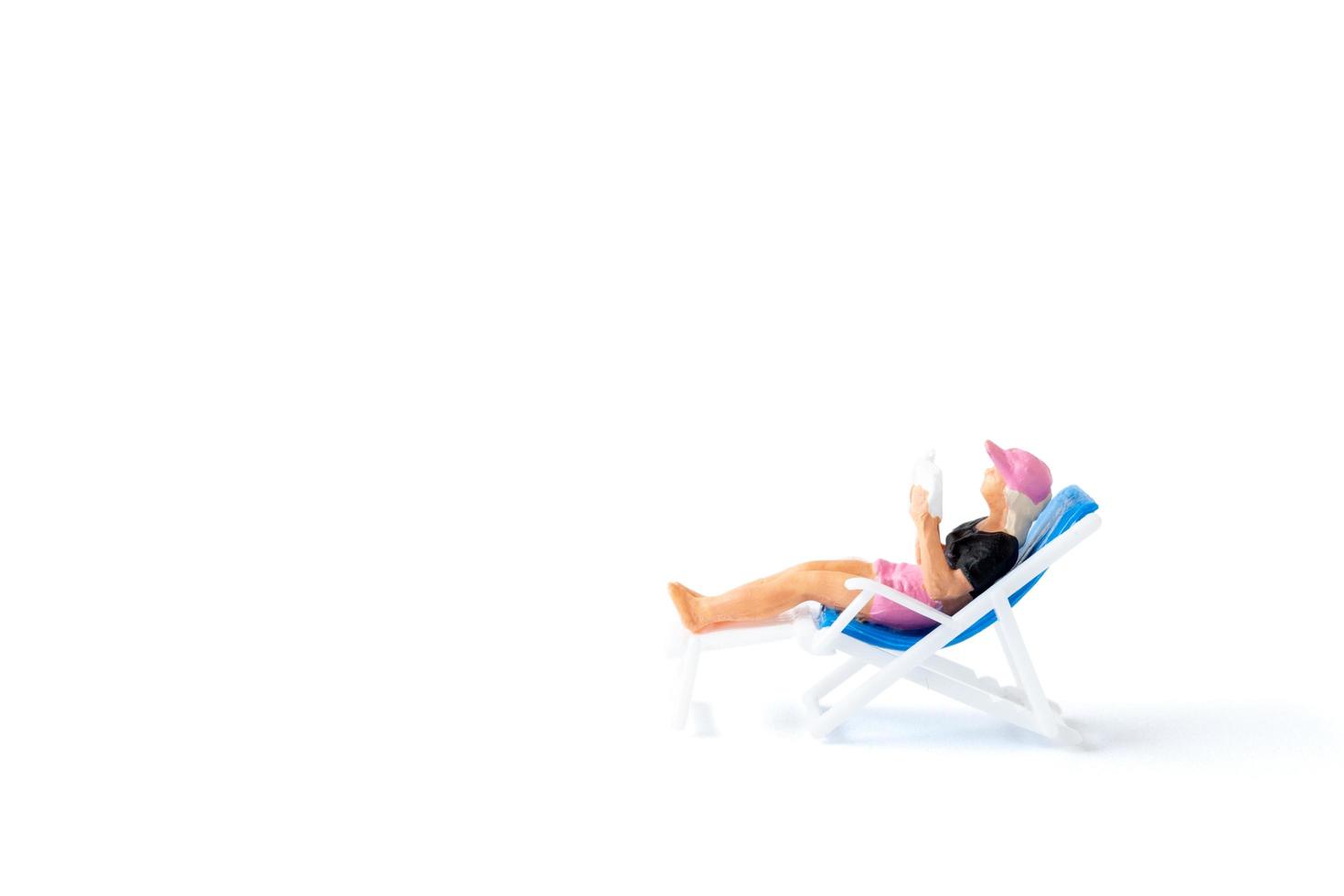 Miniature person sunbathing on a deck chair on a white background, summertime concept photo