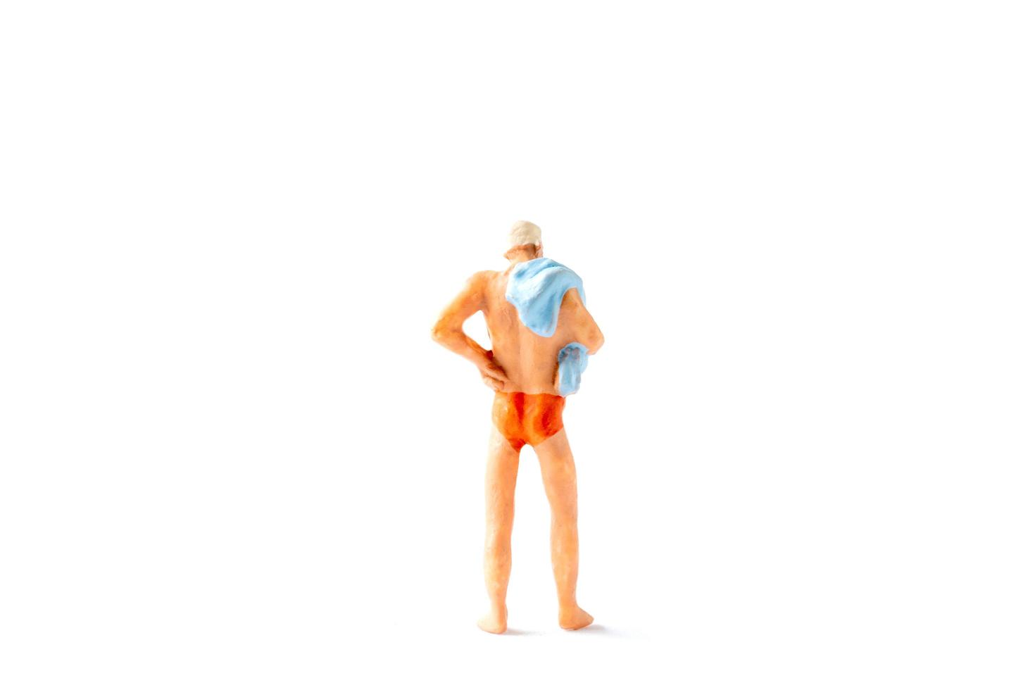 Miniature person wearing a swimsuit standing on a white background, summertime concept photo