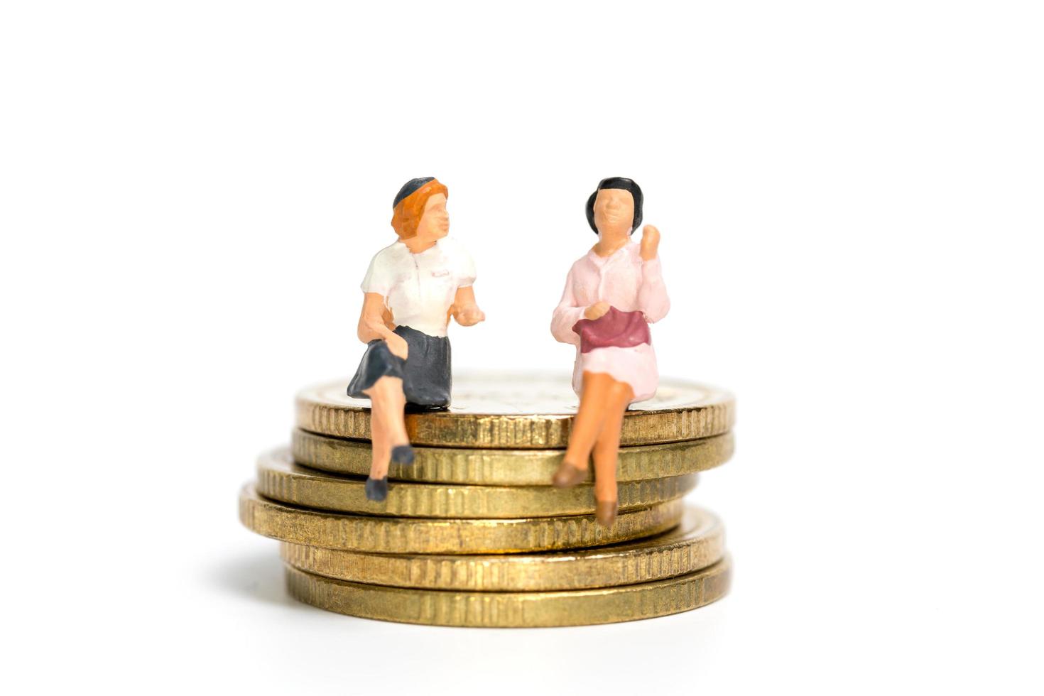 Miniature businesspeople sitting on a stack of coins, money and financial concept photo