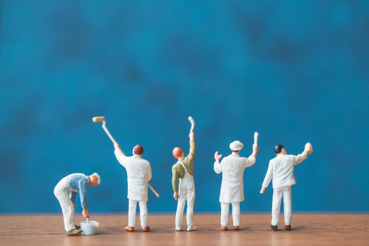 Miniature people holding brushes in front of a blue wall background photo