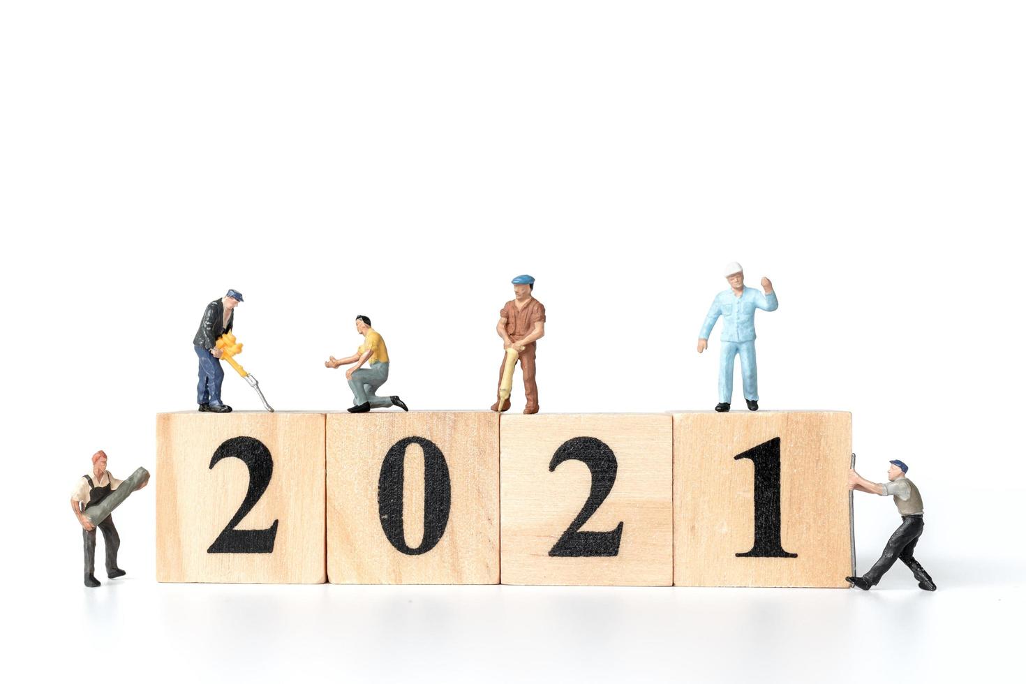 Trabajadores en miniatura que se unen para crear bloques de madera con el número 2021, concepto feliz año nuevo foto