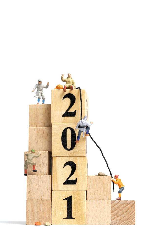 Miniature people climbing up on wooden cubes with the number 2021, Happy New Year concept photo