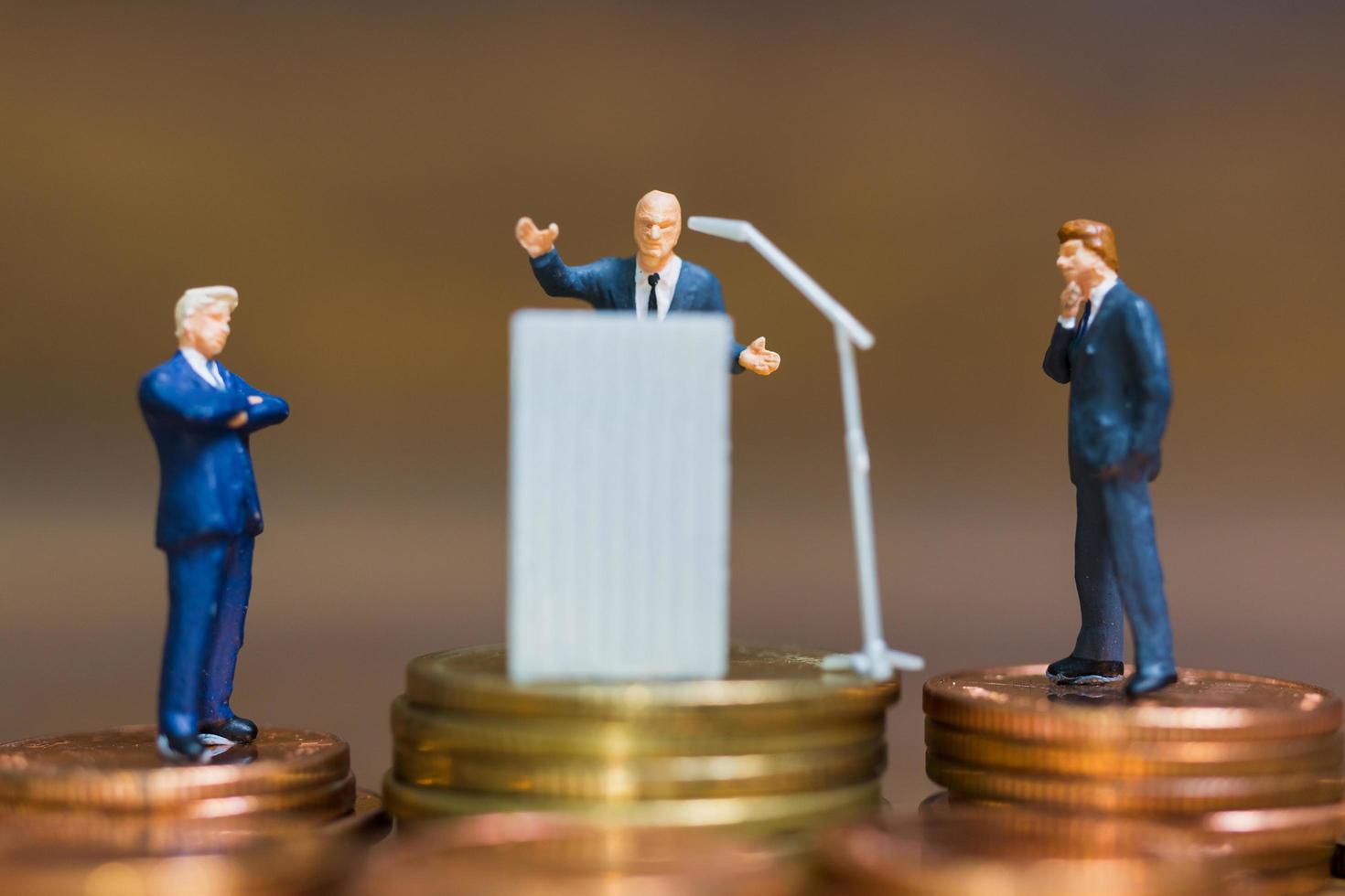 Miniature businessman speaking on a podium on a stack of coins, business and financial investment concept photo