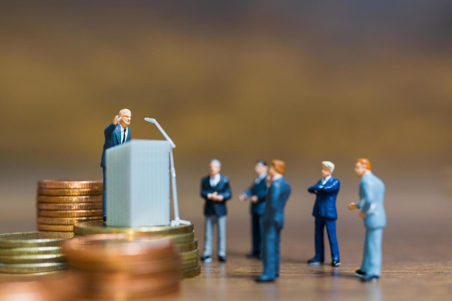 Miniature businessman speaking on a podium on a stack of coins, business and financial investment concept photo