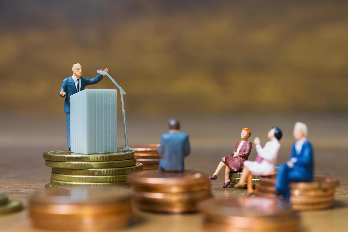 Miniature businessman speaking on a podium on a stack of coins, business and financial investment concept photo