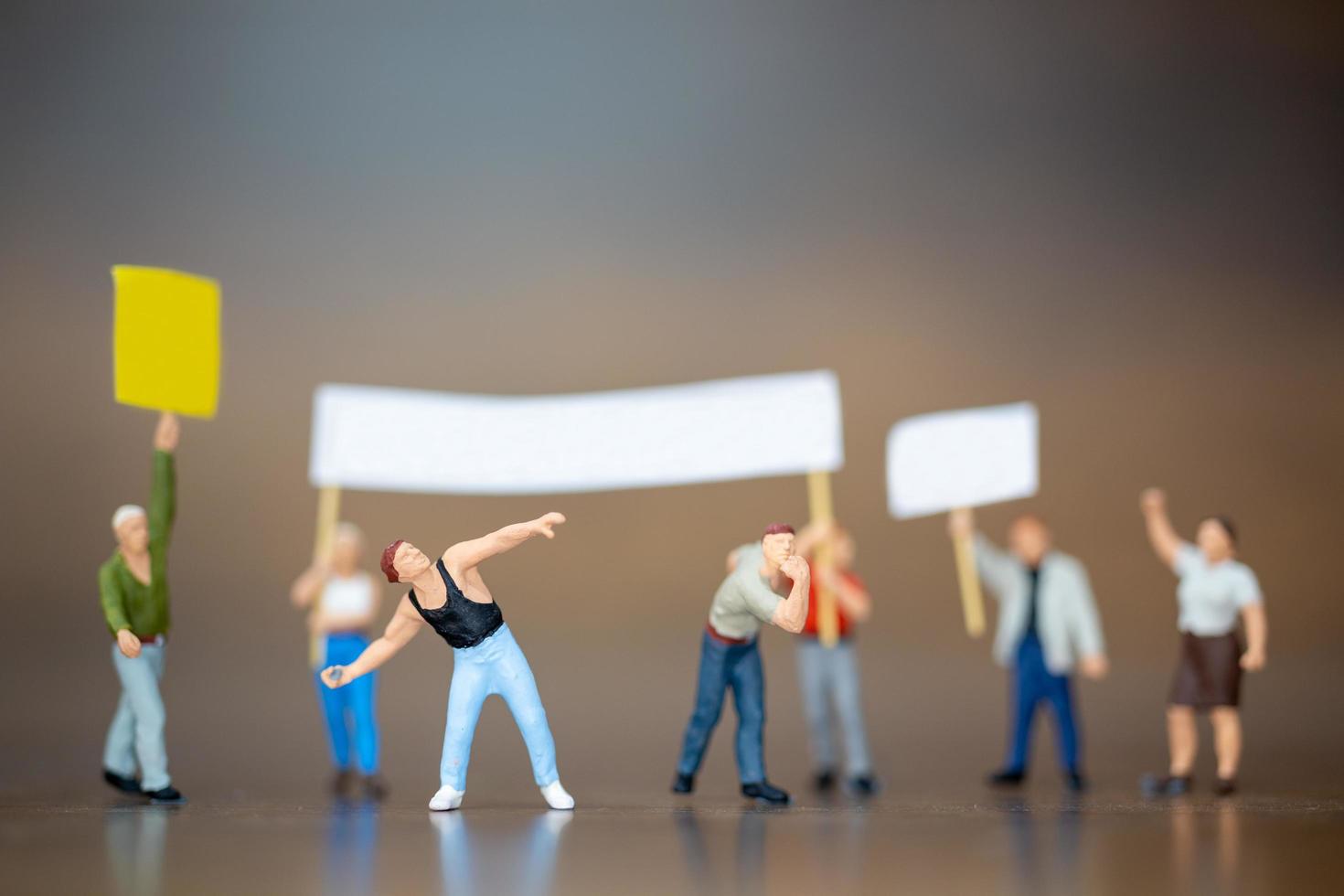 Multitud de manifestantes en miniatura levantando sus manos y gritando sobre un fondo de madera foto