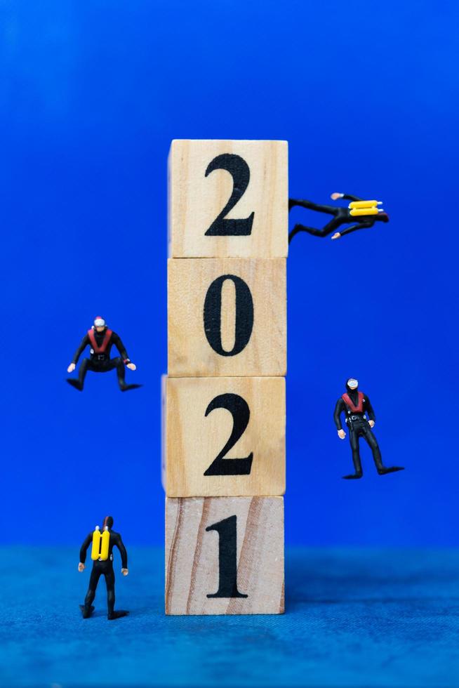 Buceadores en miniatura buceando alrededor de bloques de madera con el número 2021, concepto feliz año nuevo foto