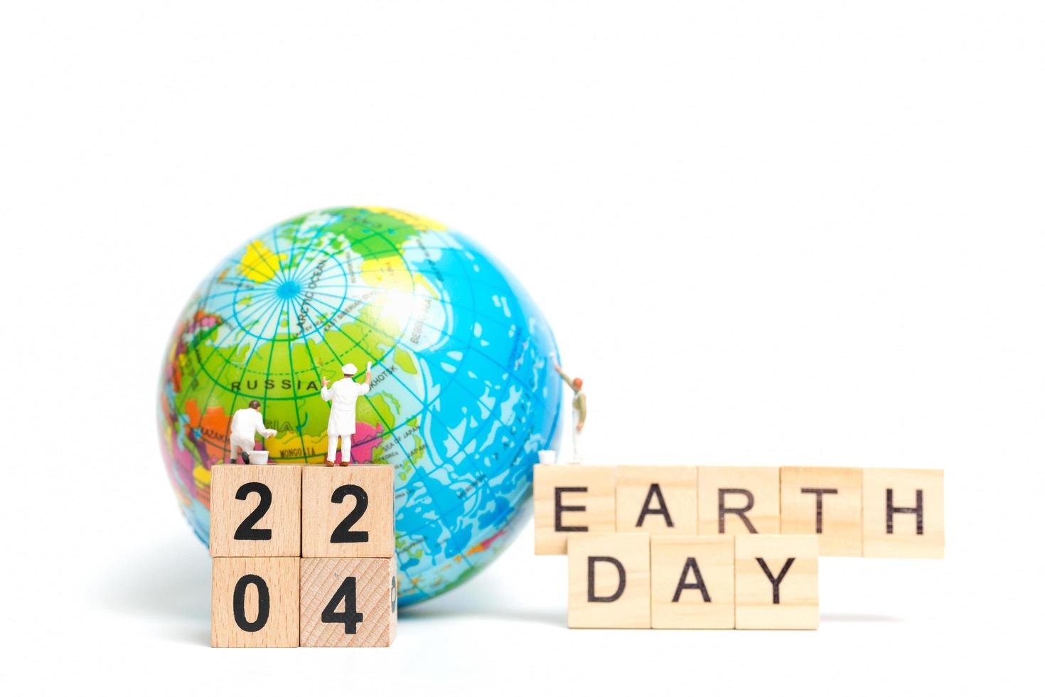 Miniature painters painting on a globe with wooden blocks showing Earth Day 22 04 on a white background, Earth Day concept photo