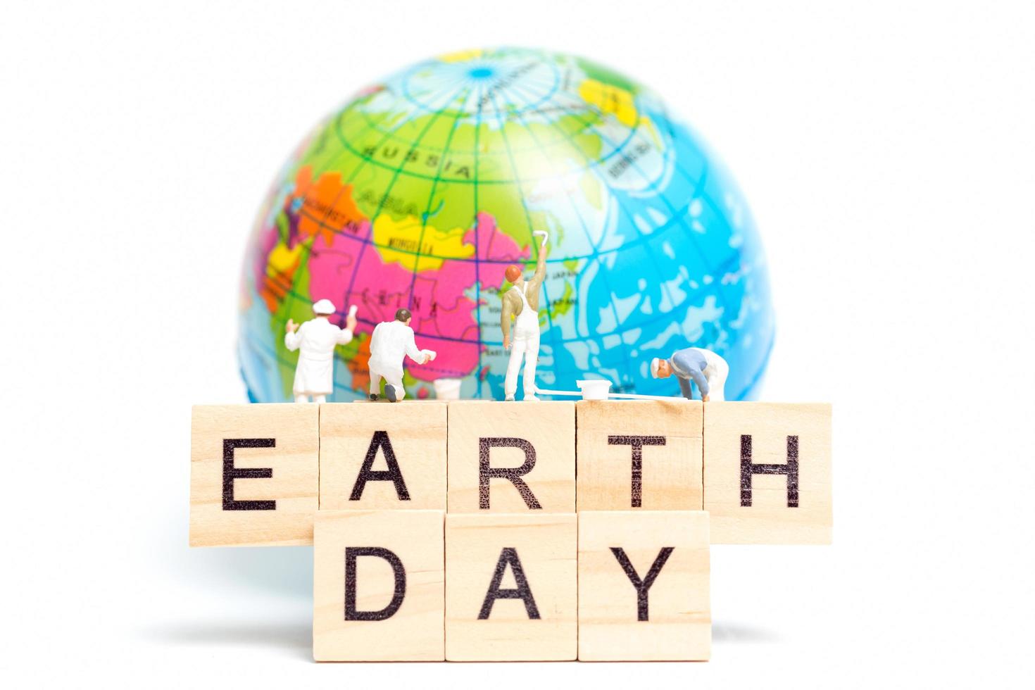 Miniature painters painting on a globe with wooden blocks showing Earth Day on a white background, Earth Day concept photo