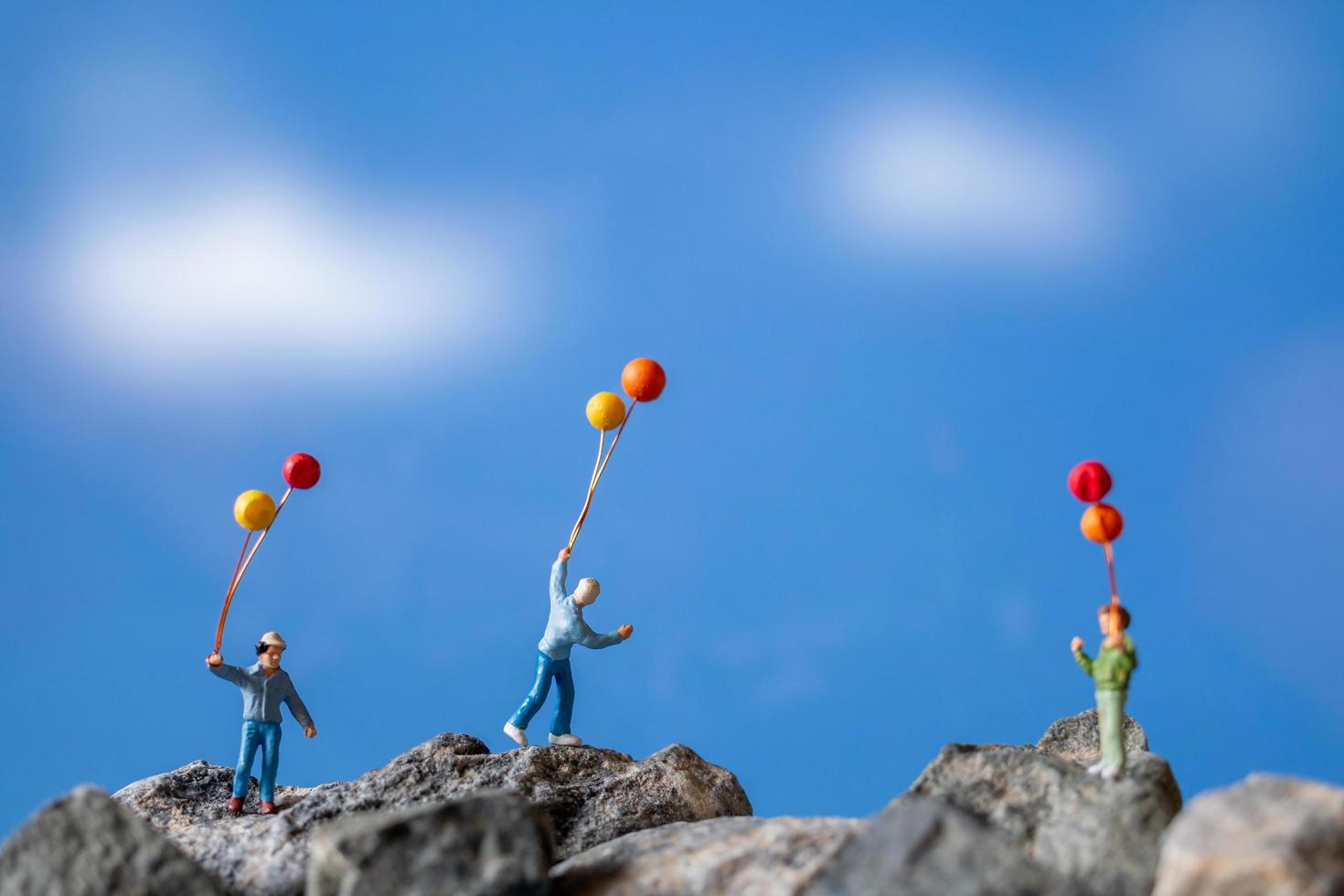 Familia en miniatura sosteniendo globos sobre una roca con un fondo de cielo azul foto