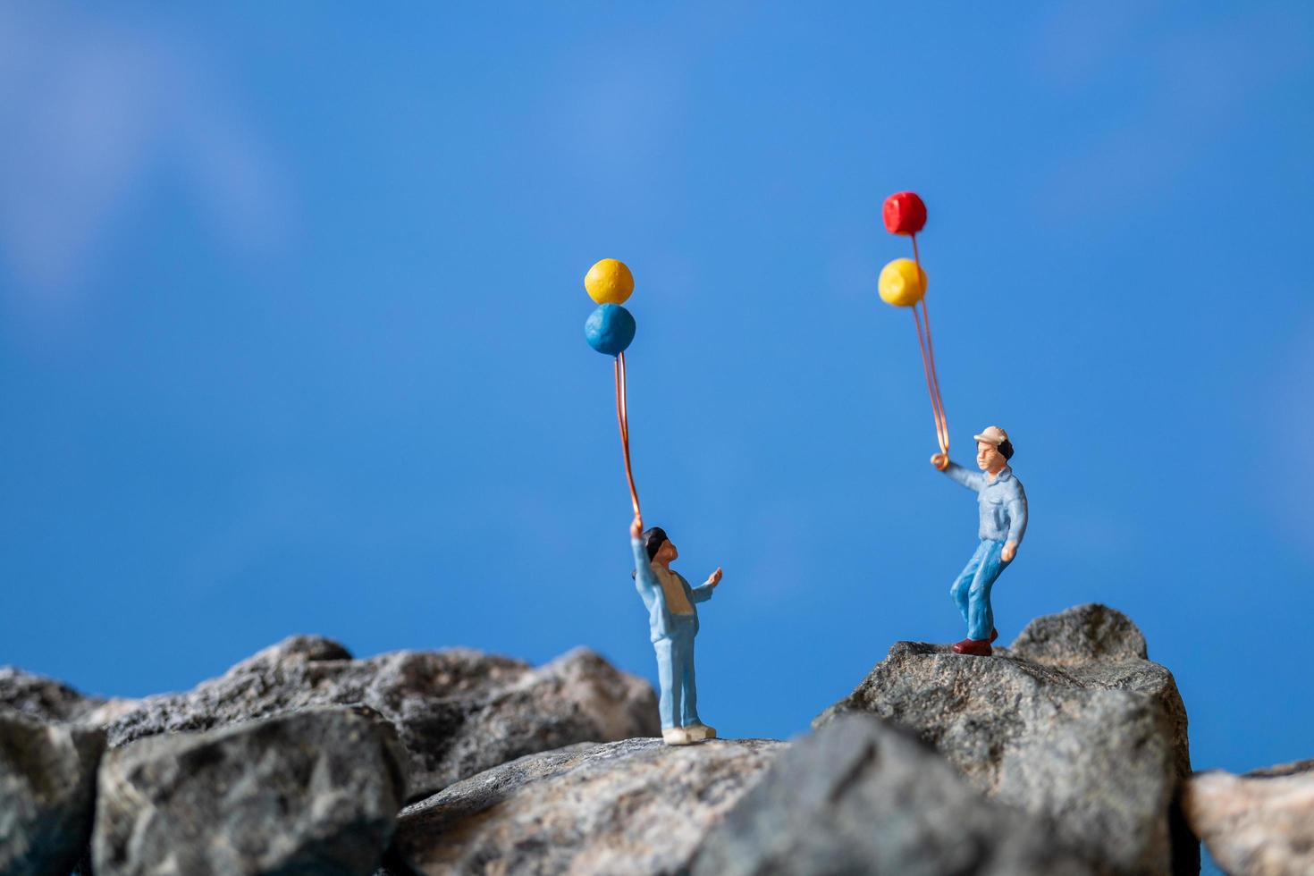 Familia en miniatura sosteniendo globos sobre una roca con un fondo de cielo azul foto
