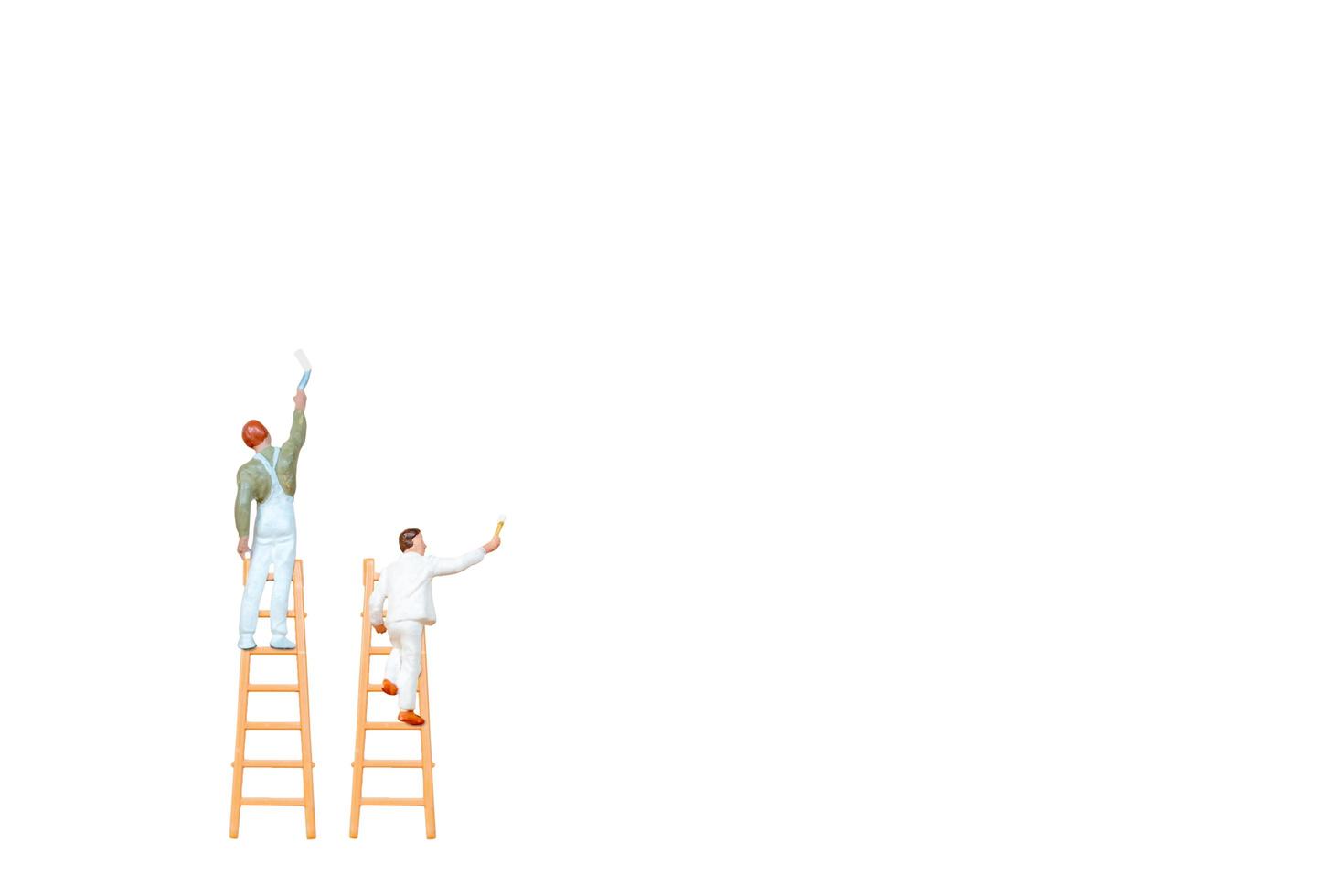 Miniature people with ladders holding brushes in front of a white wall background photo