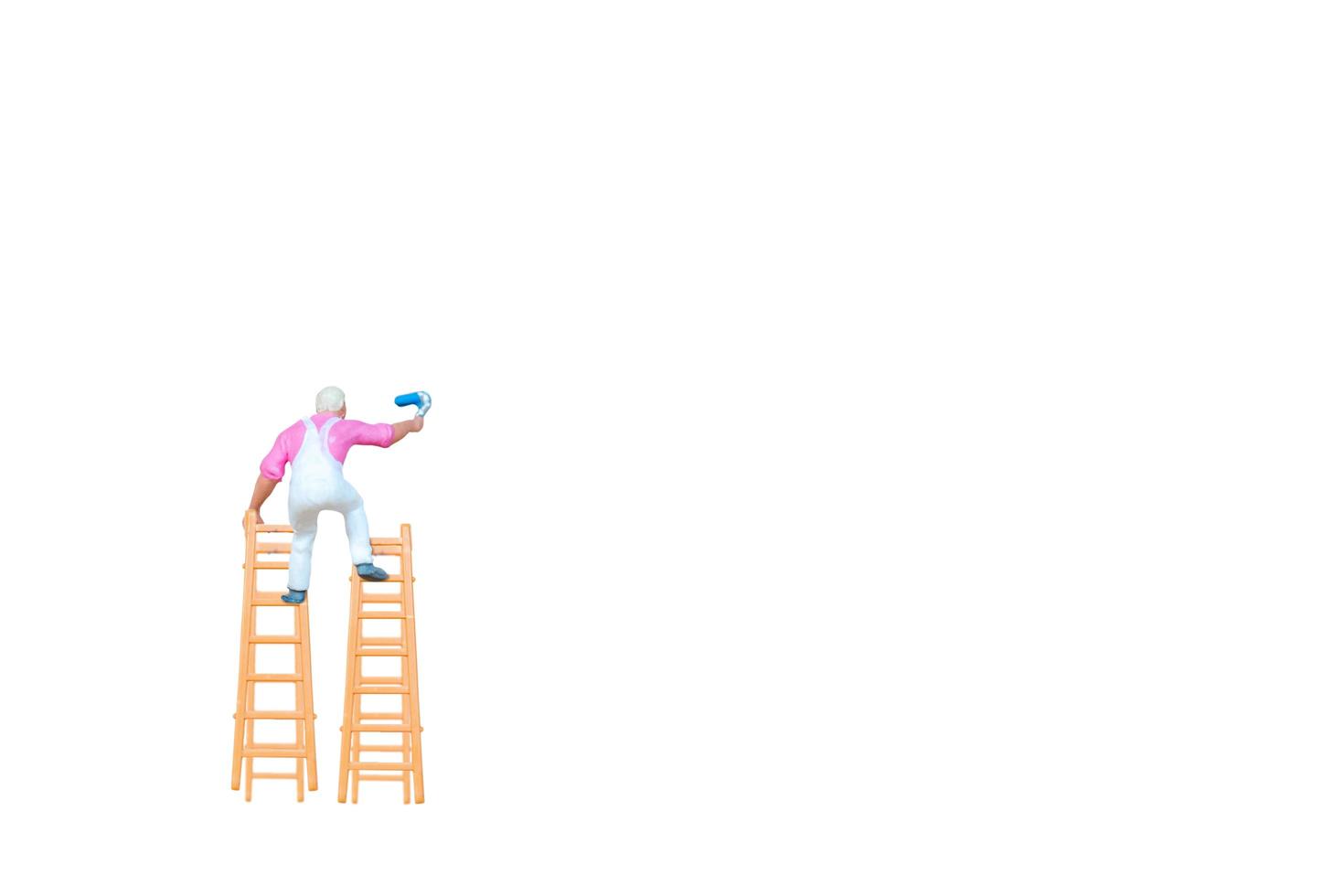 Miniature person with a ladder holding a brush in front of a white wall background photo