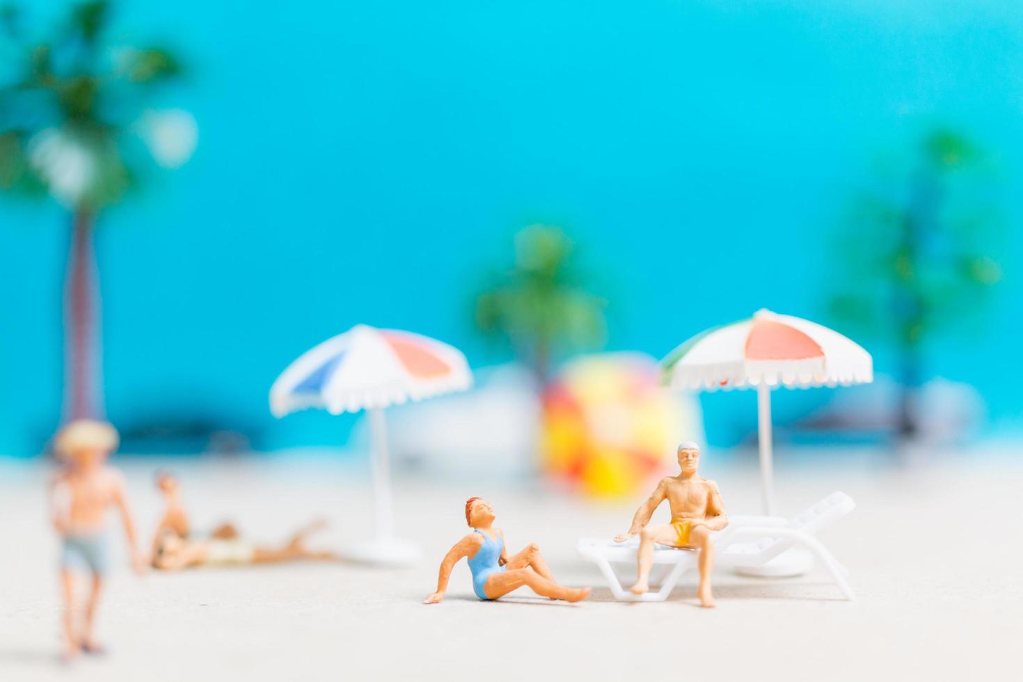 Miniature people wearing swimsuits relaxing on a beach with a blue background photo