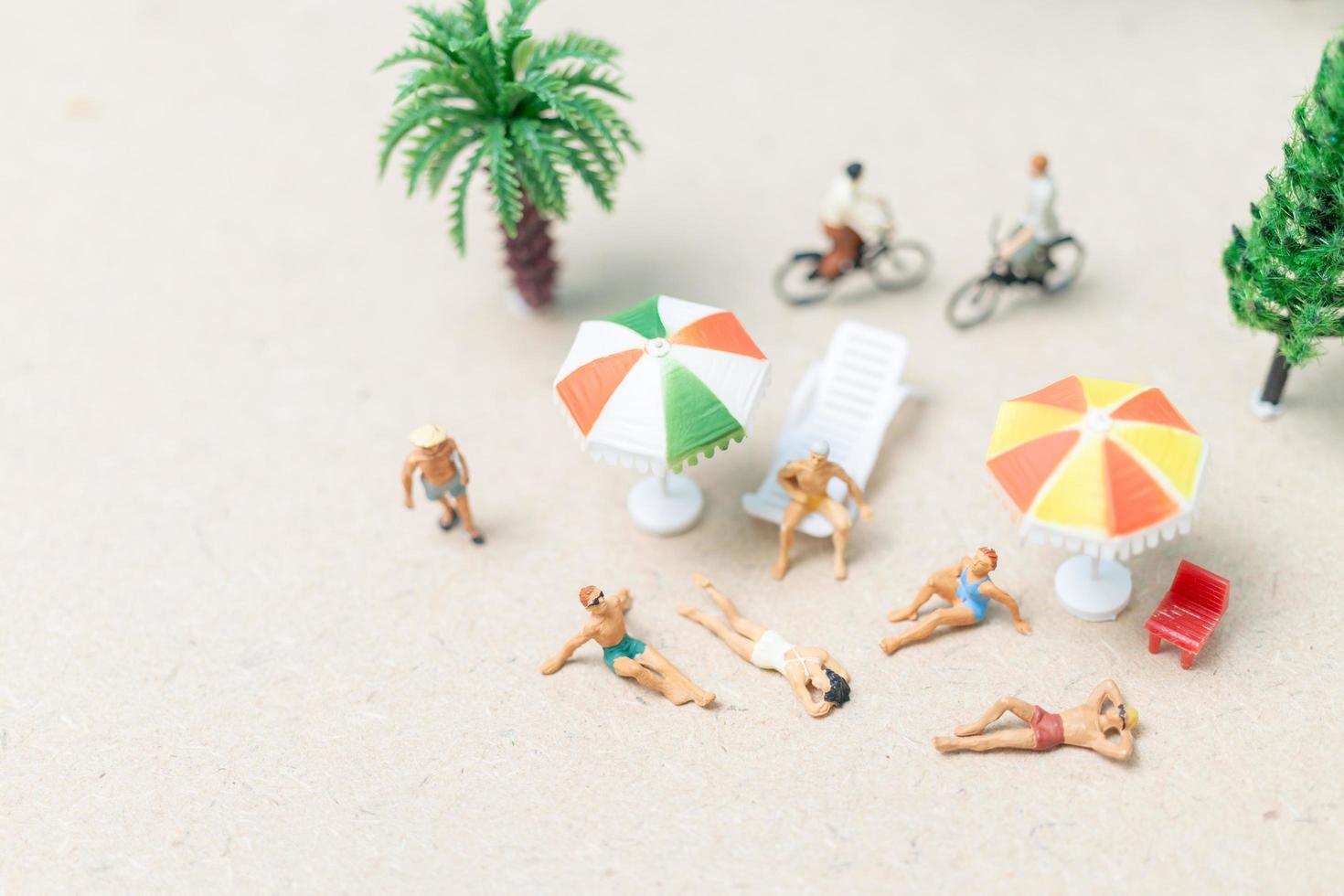 Gente en miniatura vistiendo trajes de baño relajándose en una playa con un fondo azul. foto