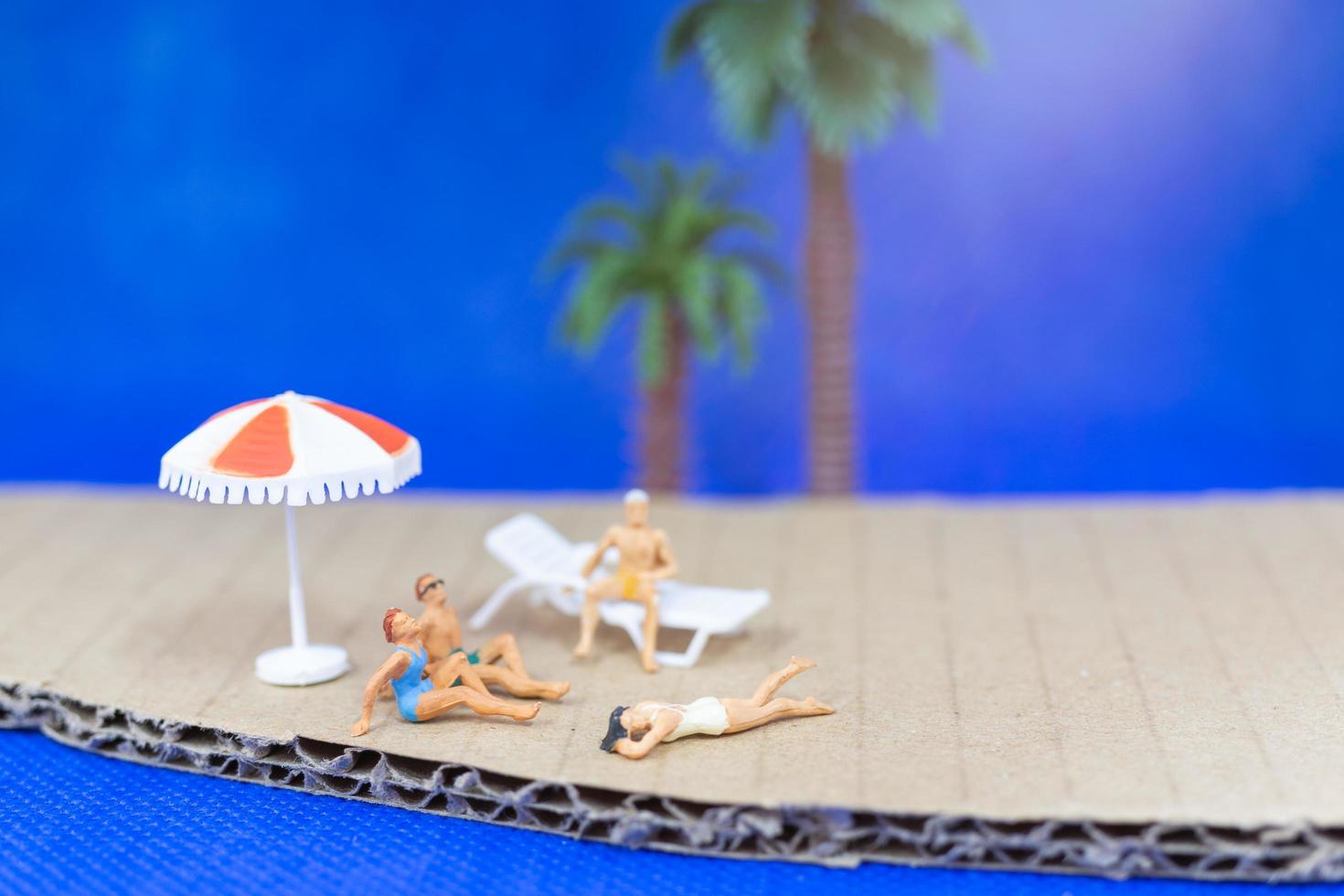 Gente en miniatura vistiendo trajes de baño relajándose en una playa con un fondo azul. foto