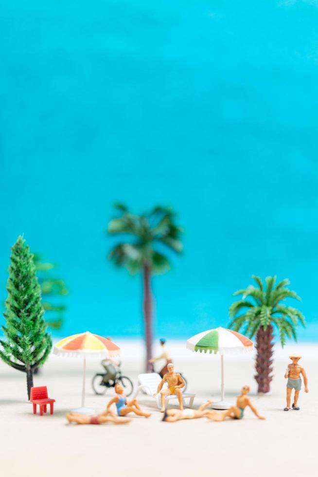 Gente en miniatura vistiendo trajes de baño relajándose en una playa con un fondo azul. foto