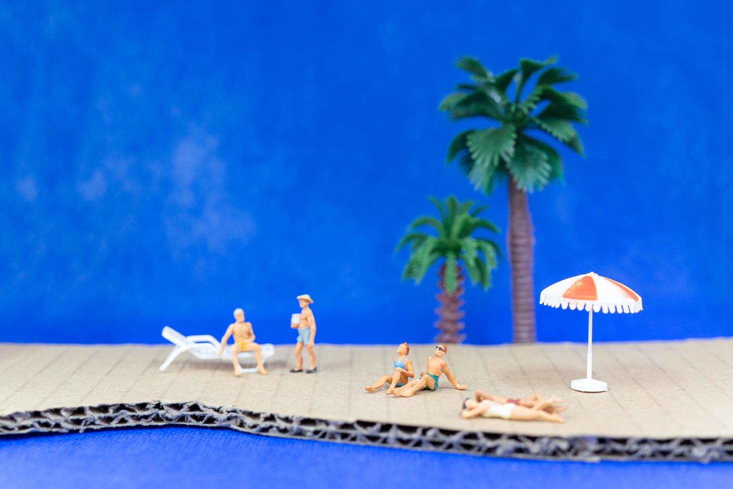 Gente en miniatura vistiendo trajes de baño relajándose en una playa con un fondo azul. foto