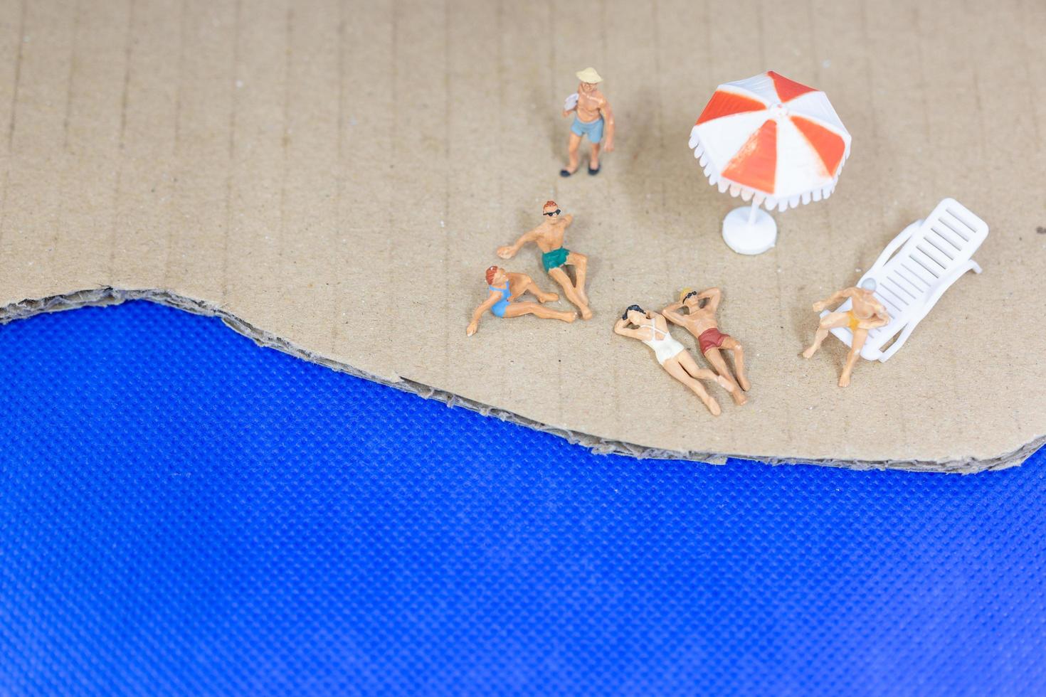 Gente en miniatura vistiendo trajes de baño relajándose en una playa con un fondo azul. foto