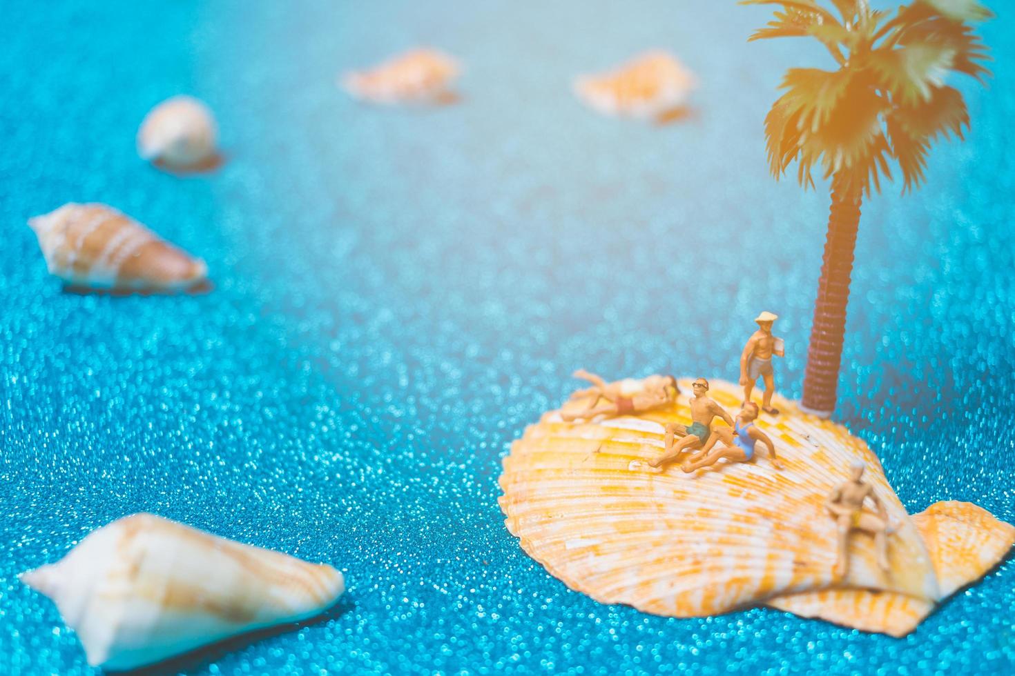 Miniature people wearing swimsuits relaxing on a seashell with a glitter background photo