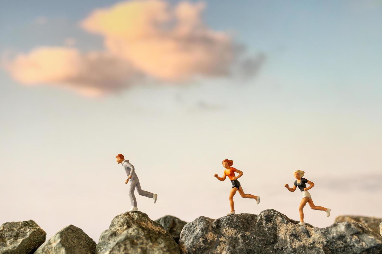 Miniature people running on a rock cliff with nature background, health and lifestyle concept photo