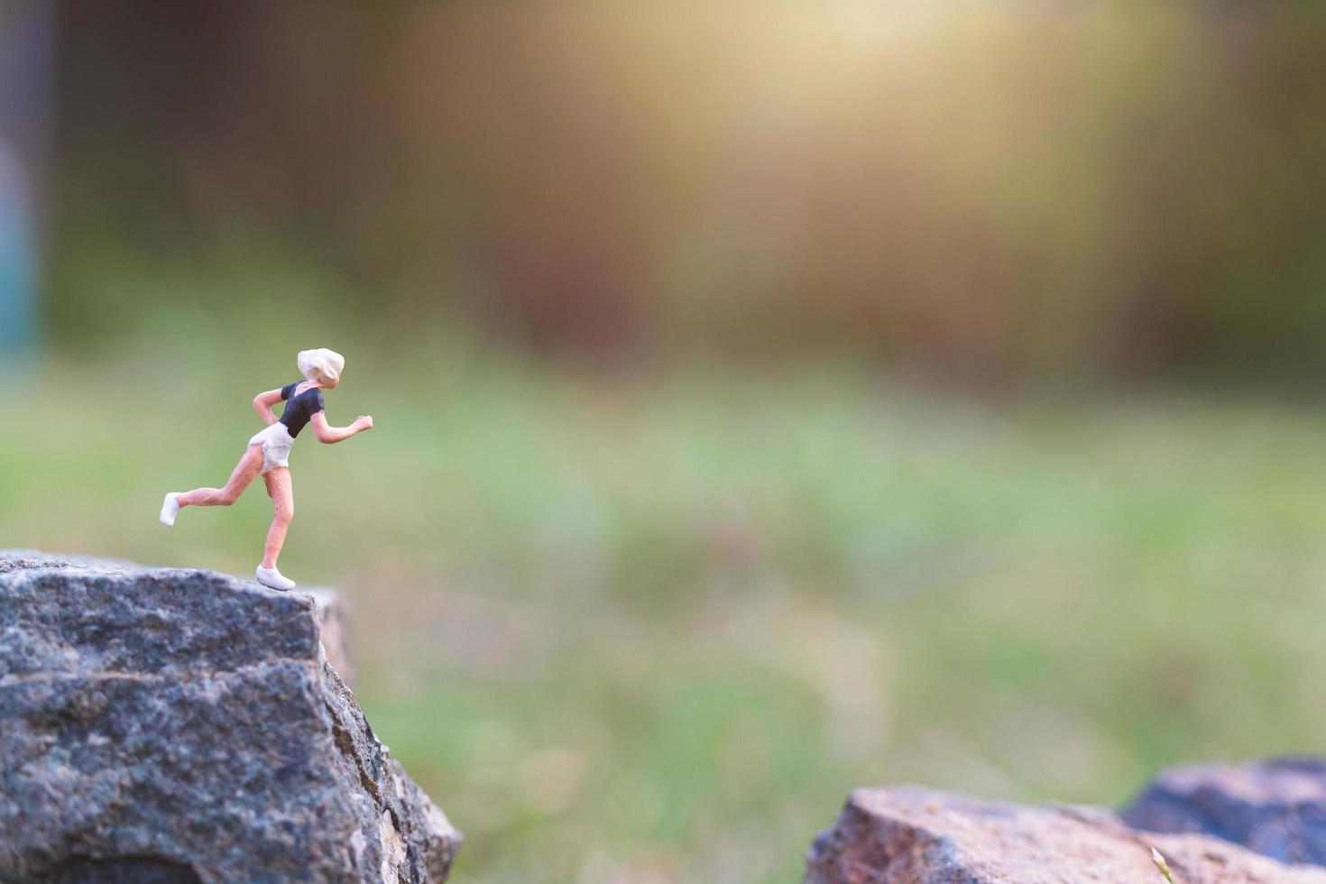 Miniature people running on a rock cliff with nature background, health and lifestyle concept photo