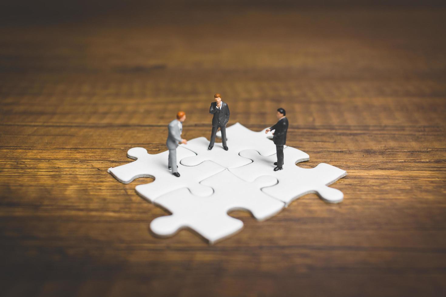 Miniature businessmen standing on jigsaws with a wooden background, business concept photo