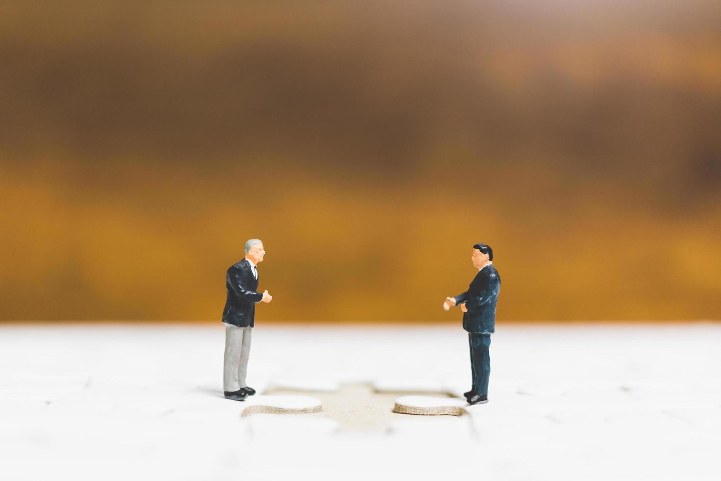 Miniature businessmen standing on jigsaws with a wooden background, business concept photo