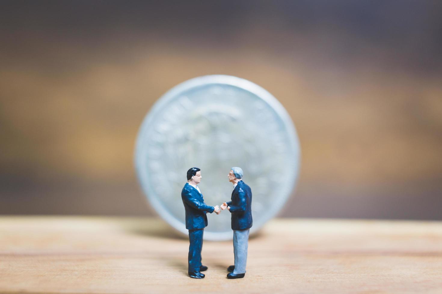 Miniature businessmen standing near a coin with a wooden background, business concept photo