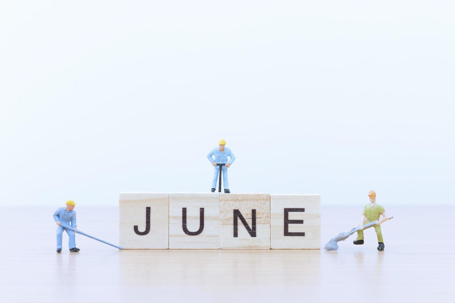 Gente en miniatura trabajando en bloques de madera con la palabra junio sobre un piso de madera foto