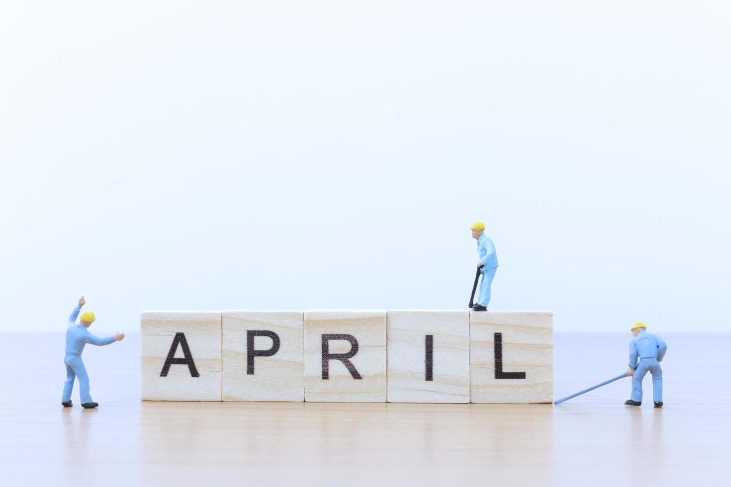 Gente en miniatura trabajando en bloques de madera con la palabra abril sobre un piso de madera foto