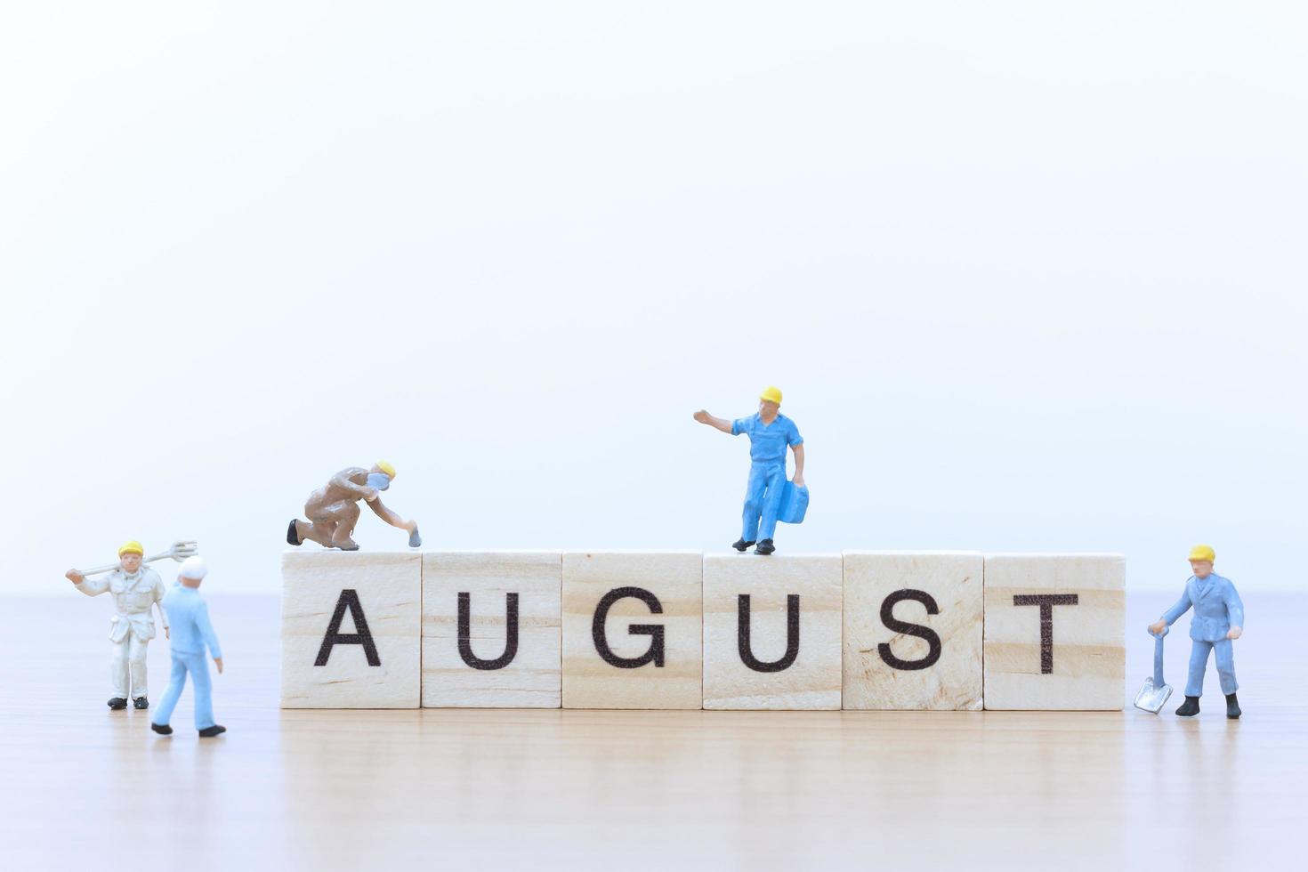 Gente en miniatura trabajando en bloques de madera con la palabra agosto sobre un piso de madera foto