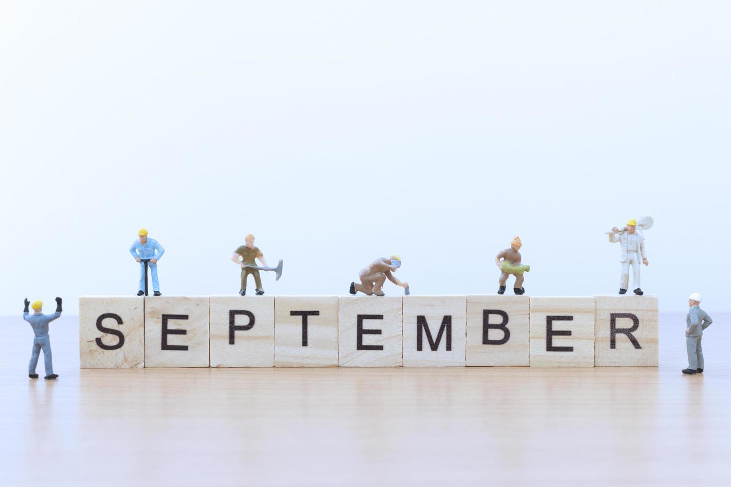 Miniature people working on wooden blocks with the word September on a wooden floor photo