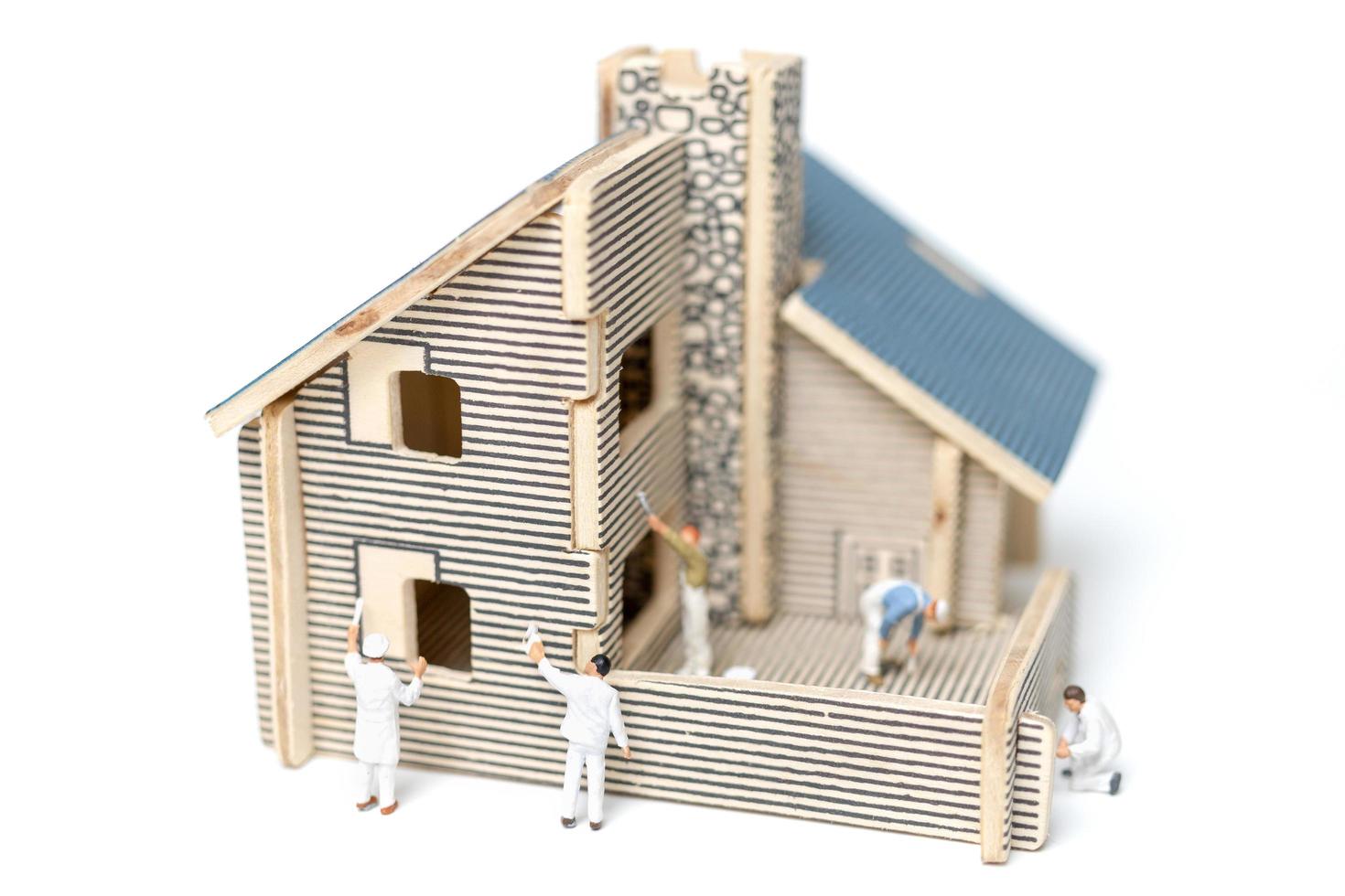 Miniature painters painting a wooden house on a white background photo