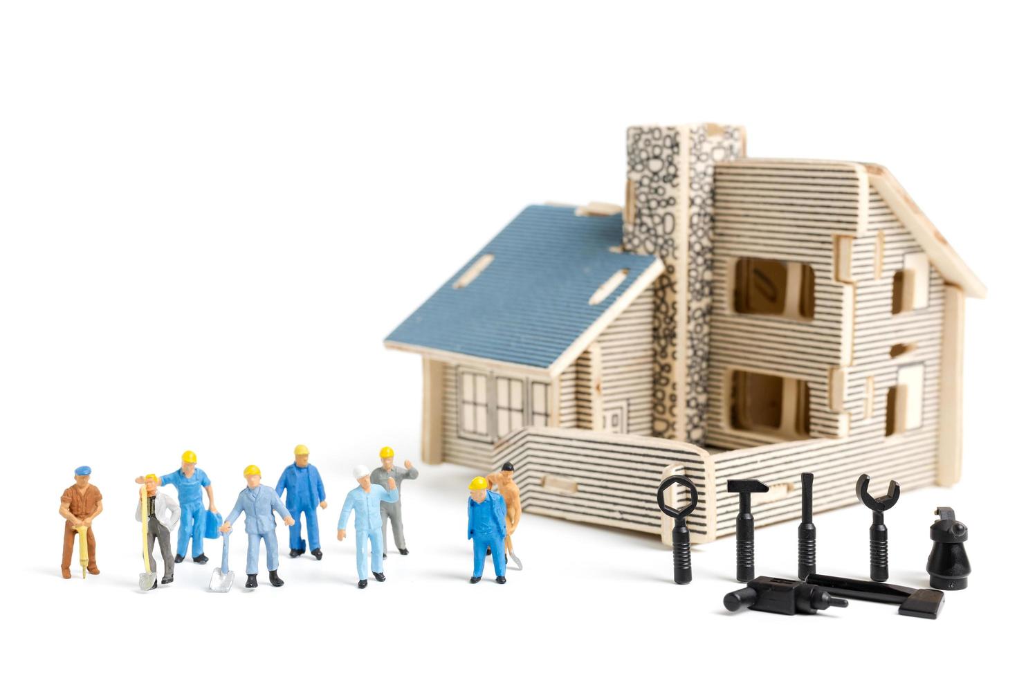 Miniature workers with tools repairing a house on a white background, construction concept photo