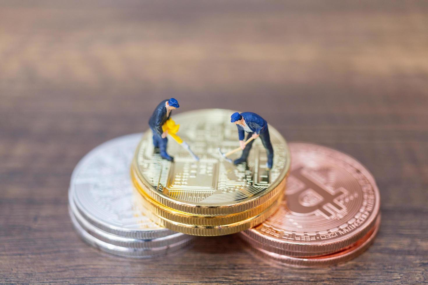 Trabajadores en miniatura haciendo criptomonedas bitcoin sobre un fondo de madera foto