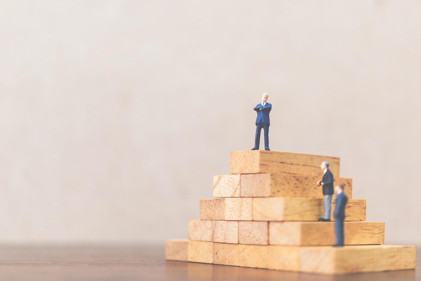 Miniature businessmen standing on a wooden block, successful business leader and teamwork concept photo