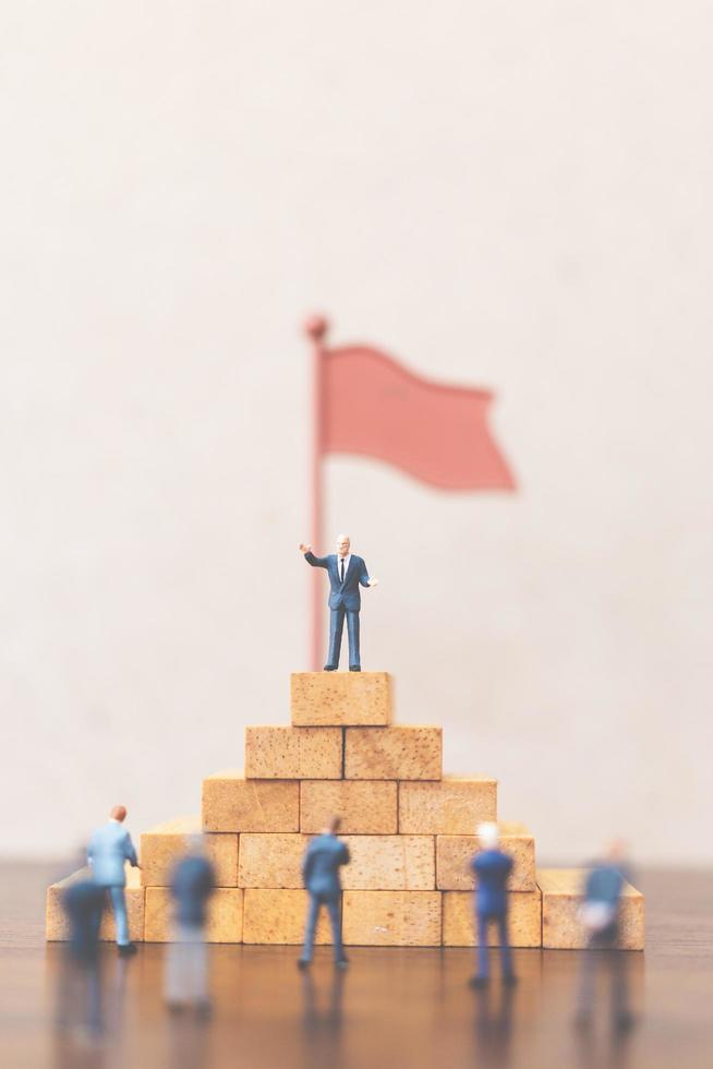 Miniature businessmen standing on a wooden block, successful business leader and teamwork concept photo