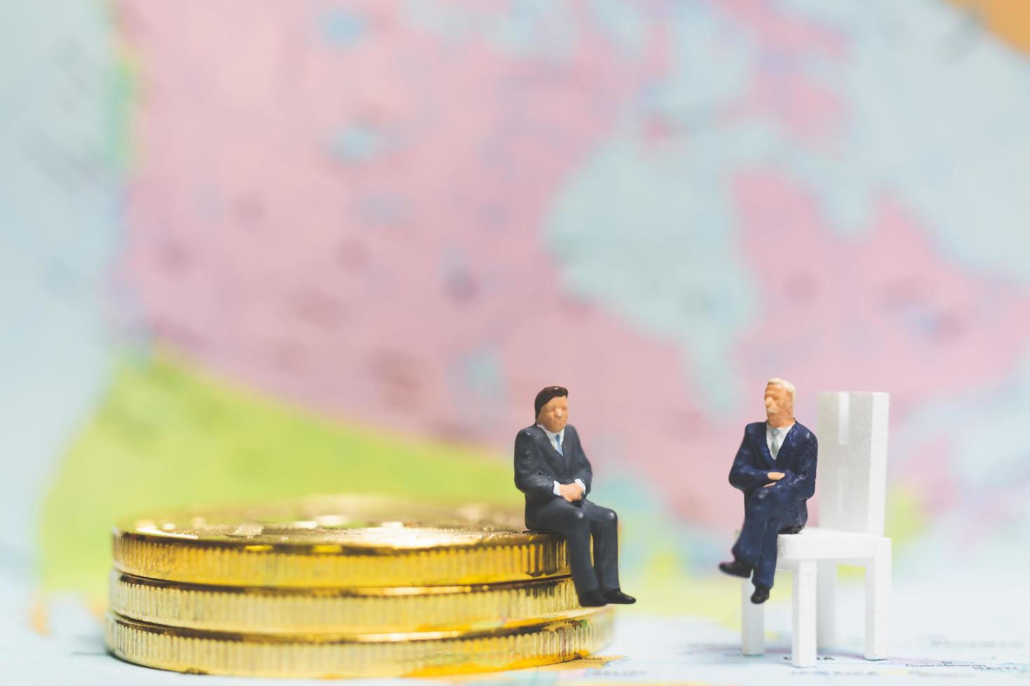 Miniature businessmen on a stack of coins with a world map in the background, money and financial business success concept photo