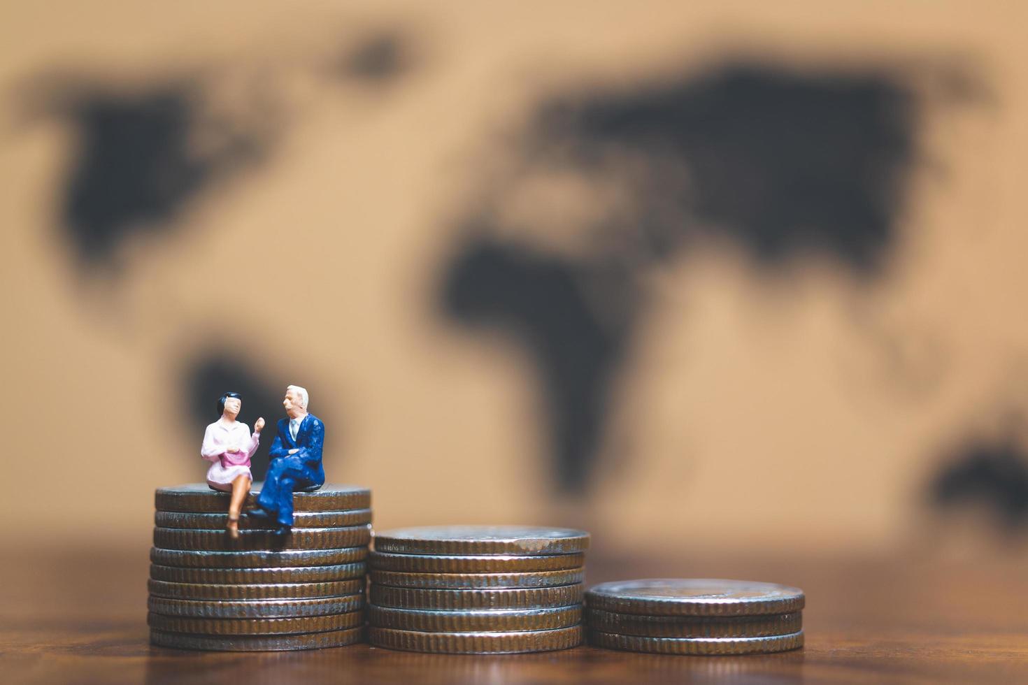 Miniature businessmen on a stack of coins with a world map in the background, money and financial business success concept photo