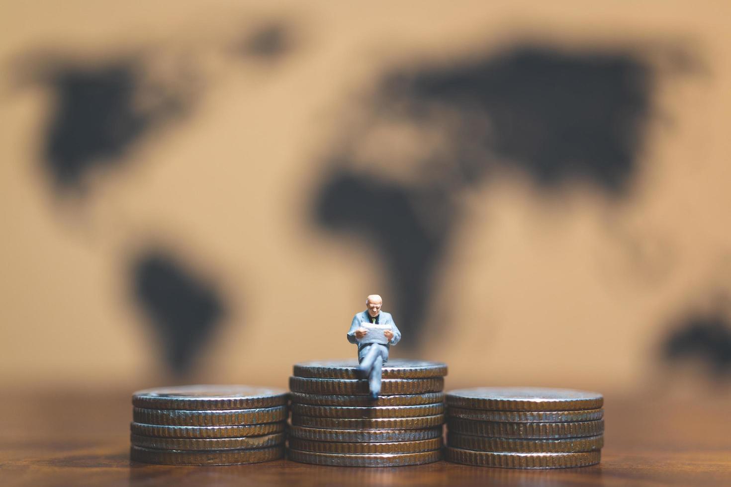 Empresario en miniatura sobre una pila de monedas con un mapa del mundo en el fondo, el dinero y el concepto de éxito empresarial financiero foto